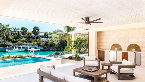 Ett modernt utomhusområde med loungekänsla, en pool, vita möbler och en takfläkt.