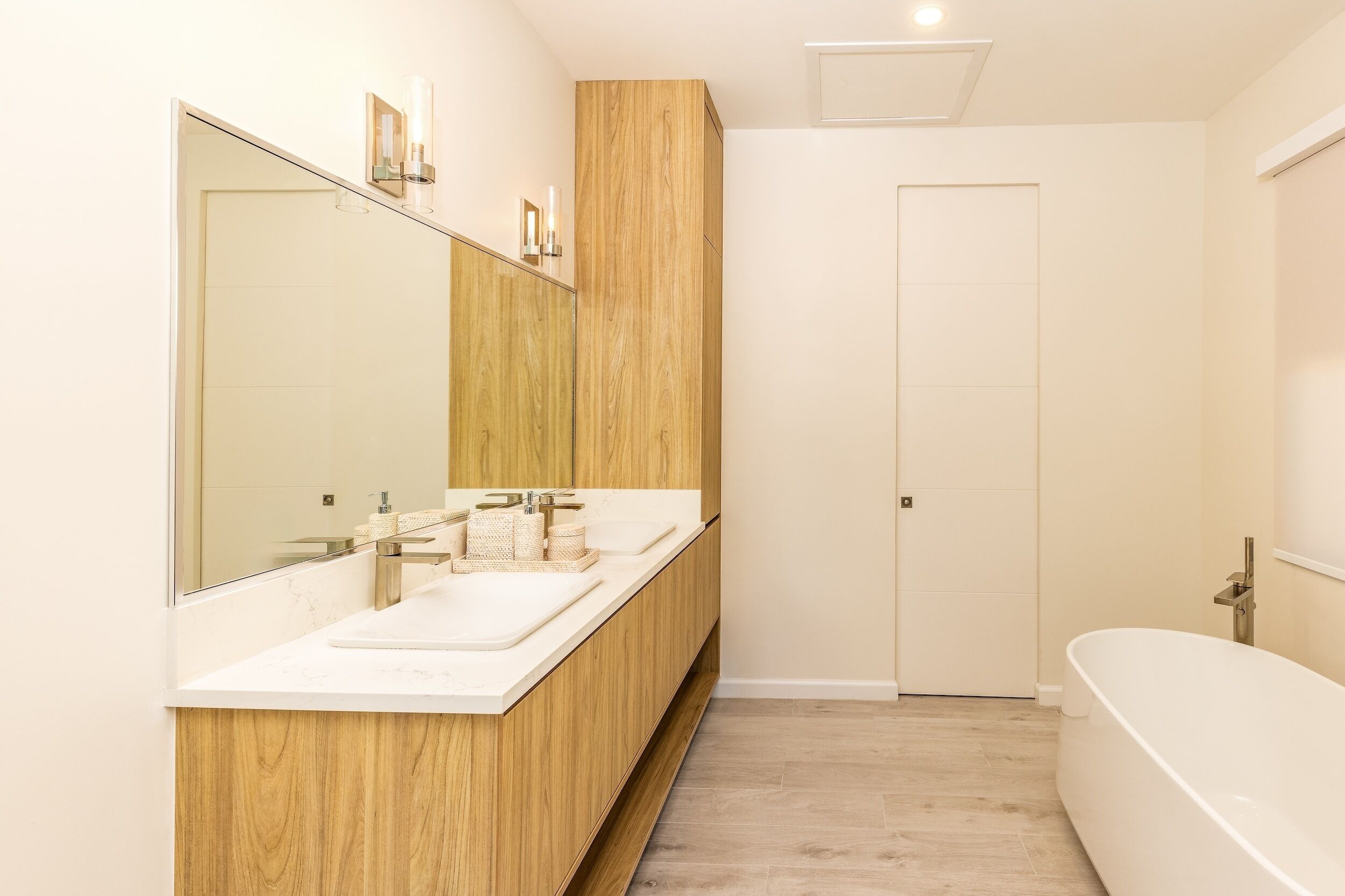 A modern bathroom with a wooden vanity, two sinks, a large mirror, and a freestanding bathtub.