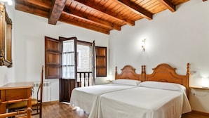 A room with two beds, wooden flooring, a wooden ceiling, a wooden desk, and a window with a view.