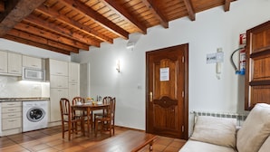 A kitchen with a washing machine, wooden dining table, and chairs, a wooden door, and a sofa in a living area.
