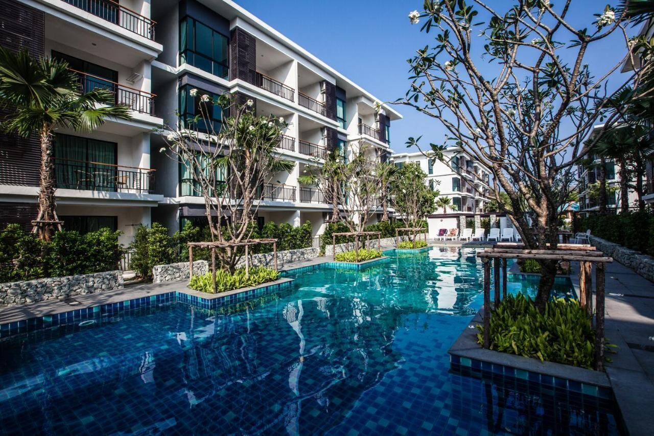 Un hôtel moderne doté d’une piscine, entouré d’une végétation luxuriante et surplombant un ciel d’un bleu éclatant.