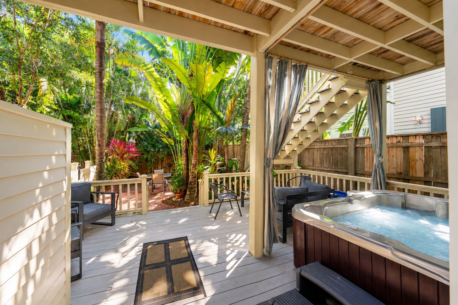 A covered outdoor area with a hot tub, seating, and a wooden deck.