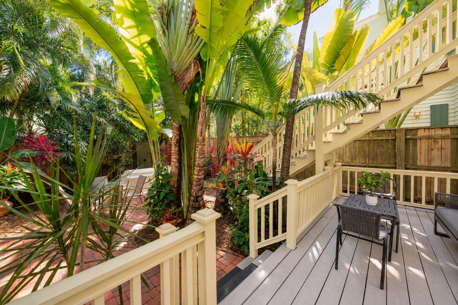 A wooden deck with a railing, surrounded by lush tropical plants and a staircase leading to an upper level.