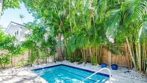 Une piscine entourée d’une végétation luxuriante et délimitée par une clôture en bois.