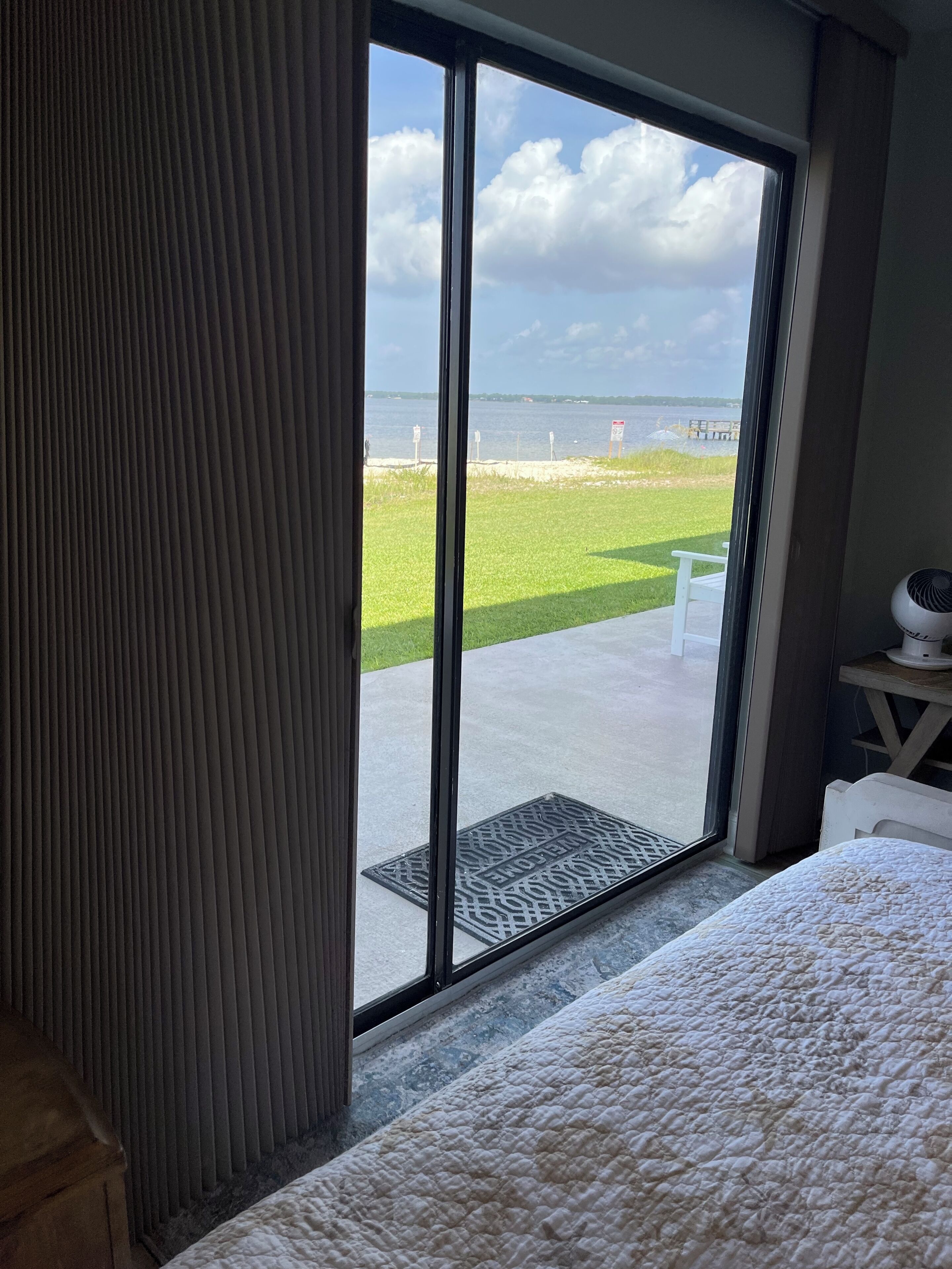 Quarto com uma grande porta de correr de vidro que dá para uma varanda com vista para uma área gramada e um corpo d'água.