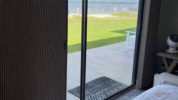 Quarto com uma grande porta de correr de vidro que dá para uma varanda com vista para uma área gramada e um corpo d'água.