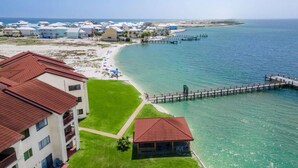 Un hotel costero con un muelle que se adentra en el mar, un área con césped y una playa con sombrillas.