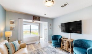 Un dormitorio moderno con una cama, dos sillones azules, una mesita de madera, un televisor y un ventanal con vistas.