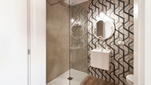 Un baño moderno con ducha envuelta en vidrio, tocador con espejo y pared con diseño.