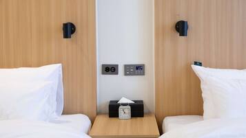 Habitación de hotel con dos camas, una mesita de noche con un reloj y una caja de pañuelos, y un panel de control en la pared.