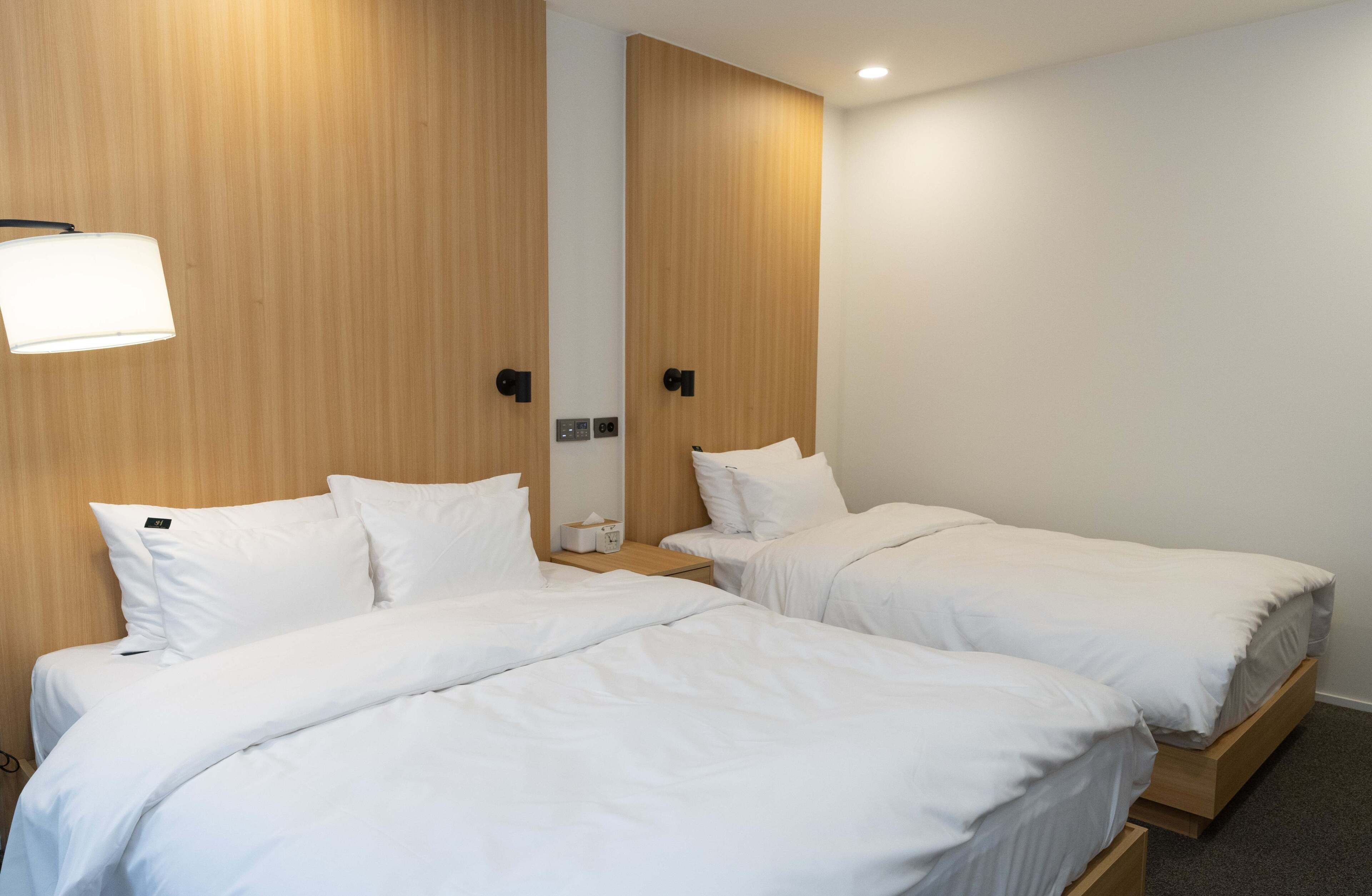 Ein Hotelzimmer mit zwei Einzelbetten, einem Nachttisch mit Lampe und einer an der Wand montierten Steuerung.