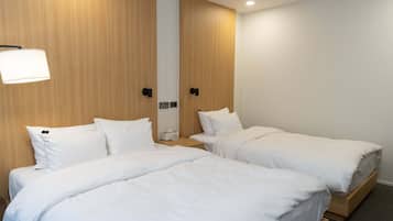 Ein Hotelzimmer mit zwei Einzelbetten, einem Nachttisch mit Lampe und einer an der Wand montierten Steuerung.