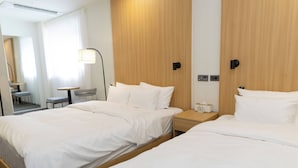 Una habitación de hotel con dos camas, una mesita de noche con lámpara, una pequeña mesa con silla y un espejo.