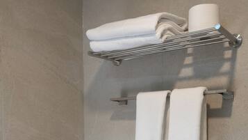 Un baño con un perchero con toallas dobladas, una cesta con toallas adicionales y un secador de pelo en un estante.
