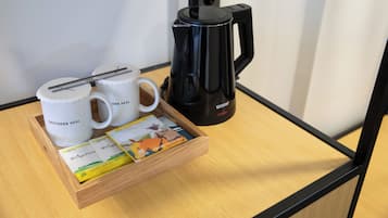 Un plateau avec deux tasses blanches, une machine à café noire et un livre, le tout posé sur une table en bois.
