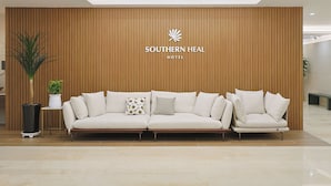 Un área de recepción con pared de paneles de madera, un sofá con varios cojines, una planta en maceta y un cartel que dice 'Southern Heal Hotel'.