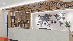 Un mostrador de recepción con un mapa mundial y relojes que marcan diferentes husos horarios. Hay estantes con libros y objetos decorativos.