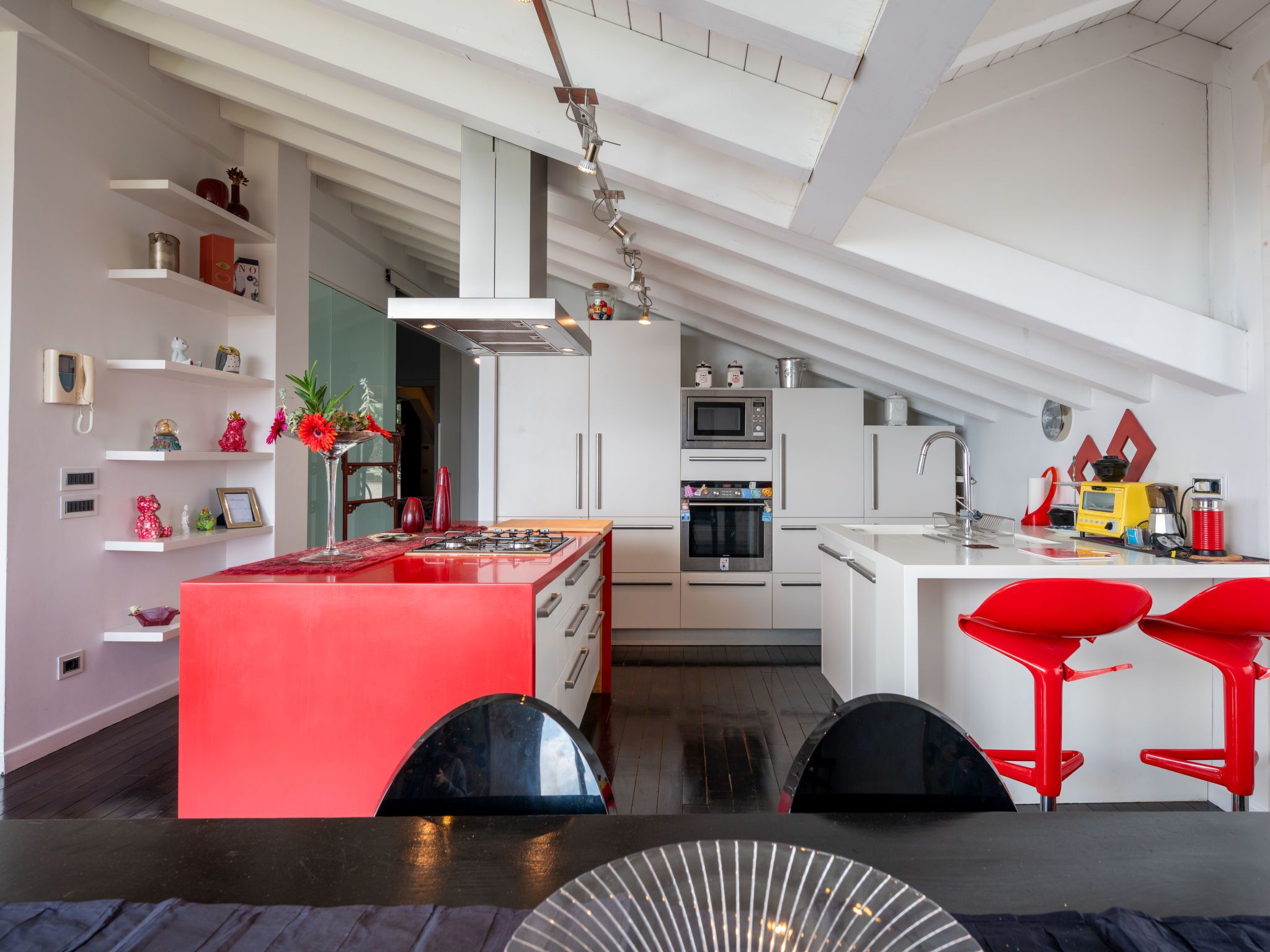 A modern kitchen with white cabinetry, a red island, and red bar stools.