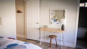 Un dormitorio con cama, escritorio, taburete, espejo y puerta.