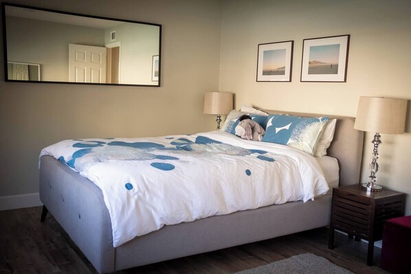A bedroom with a bed, two bedside lamps, a nightstand, a mirror, and two framed pictures on the wall. - Spacious 4-Bedroom Pool House - 10 Mins to Disneyland - AC, Fast WiFi, BBQ (Anaheim)