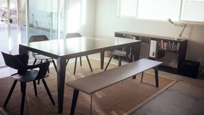 Una habitación moderna con una mesa grande, sillas, un banco, una estantería y un radiador.