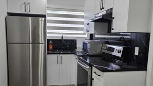 A modern kitchen with stainless steel appliances, white cabinetry, and a black countertop. - Cozy 1BR Suite, Sleeps 3, Private Entry + Parking (Calgary)