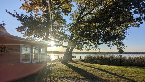 A lakeside cabin with a large window overlooking the water, a picnic table, and a 'Road Closed' sign in the background.