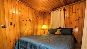 A wooden-paneled room with a bed, a lamp, and a teddy bear.
