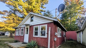 A small, single-story red wooden house with a white door and windows, a satellite dish on the roof, and a small porch.
