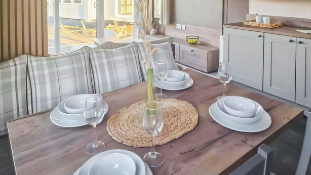 Une table à manger dressée avec de l’assiette blanche, des verres et un vase rempli de fleurs.