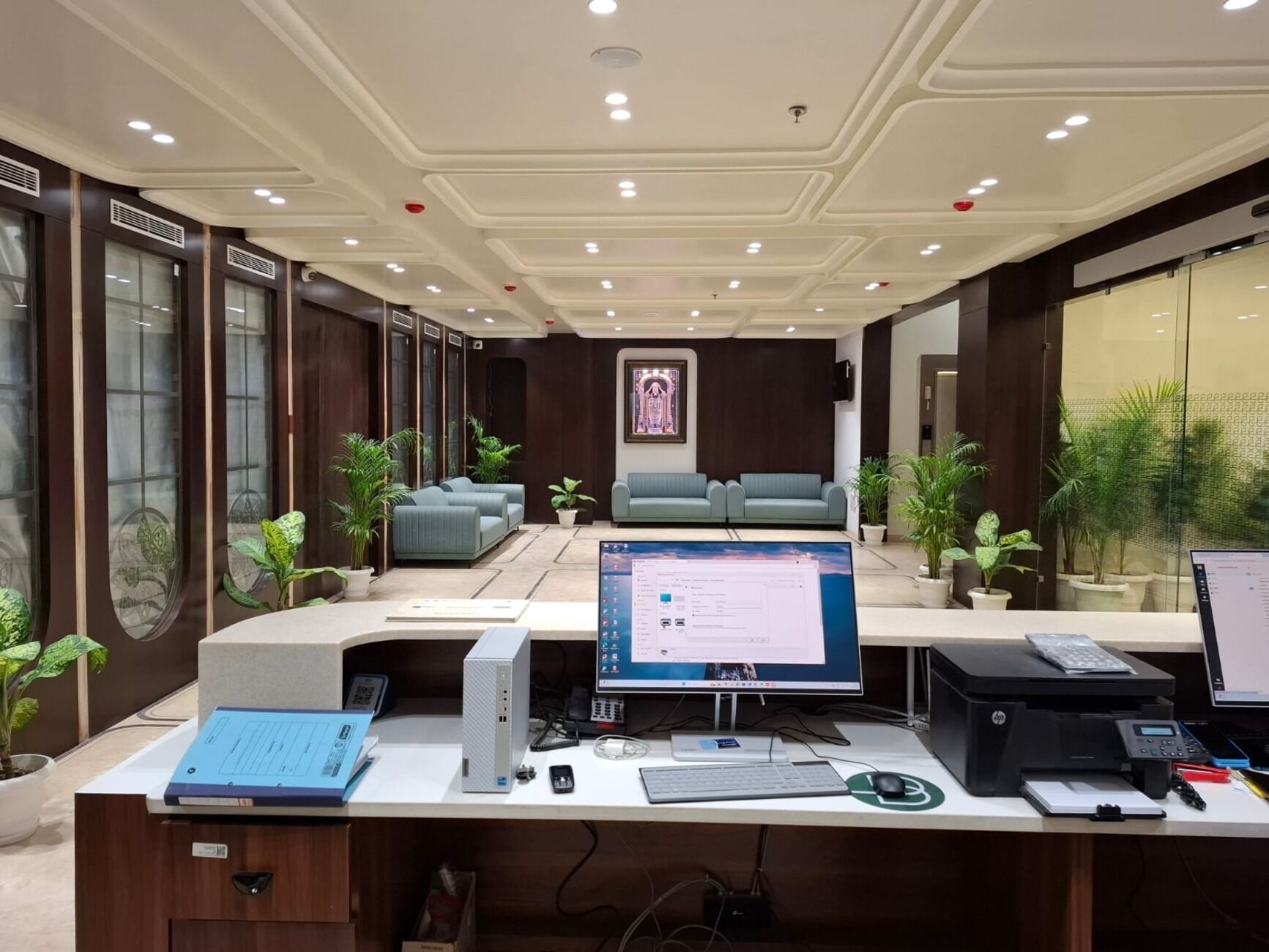 Un espacio de oficina moderno con mostrador de recepción, computadora, impresora y zona de estar.