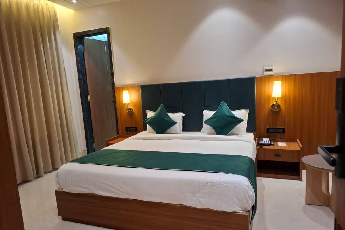 A hotel room with a large bed, two bedside tables, a wooden headboard, and a small desk with a chair.