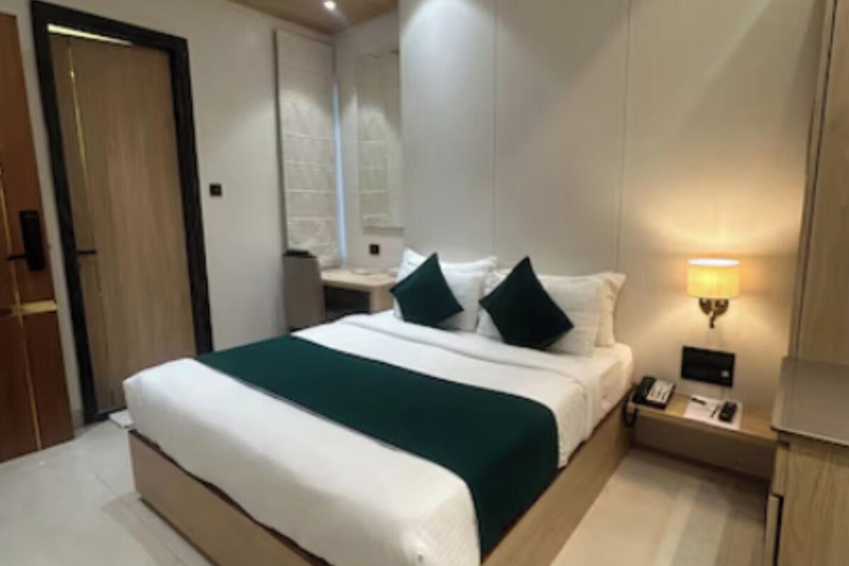 A modern hotel room with a large bed, bedside tables, a nightstand, and a wall-mounted lamp.