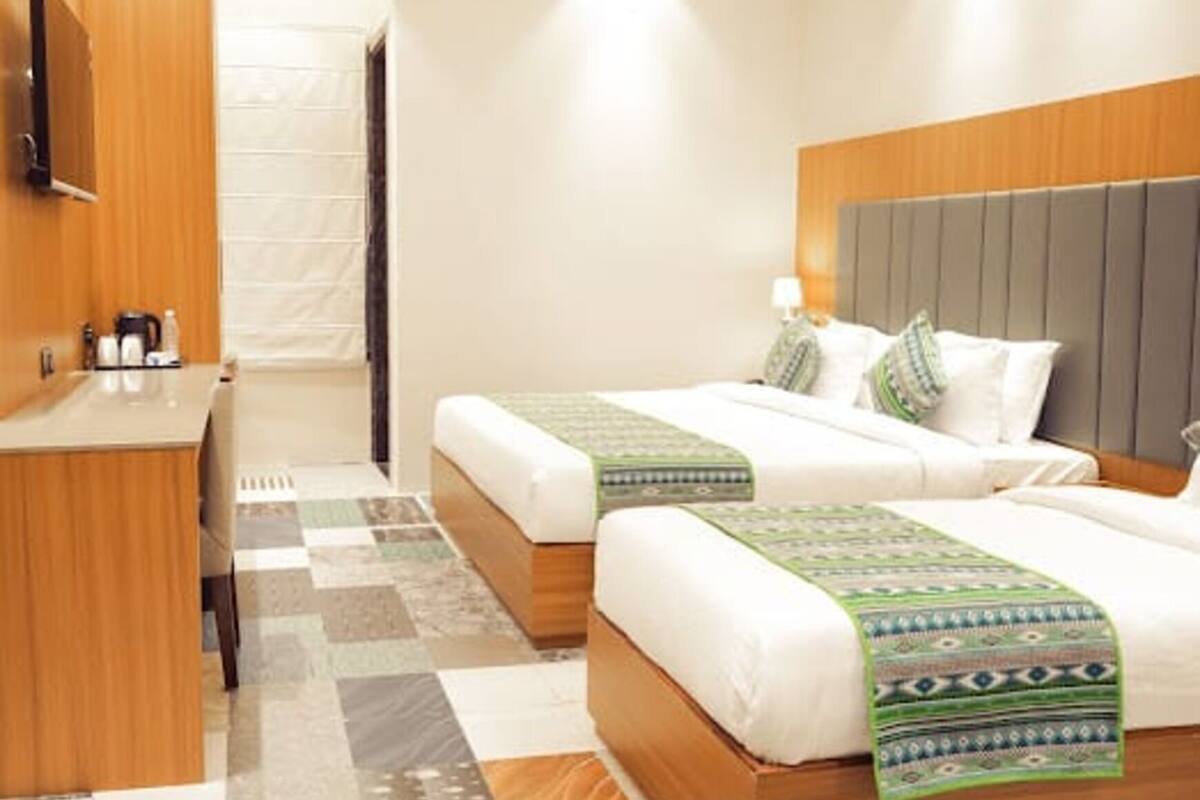 A hotel room with two beds, a wooden headboard, a small desk with a mirror, and a check-in counter.