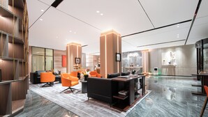 A modern hotel lobby with a marble floor, a reception desk, and seating areas with orange chairs.