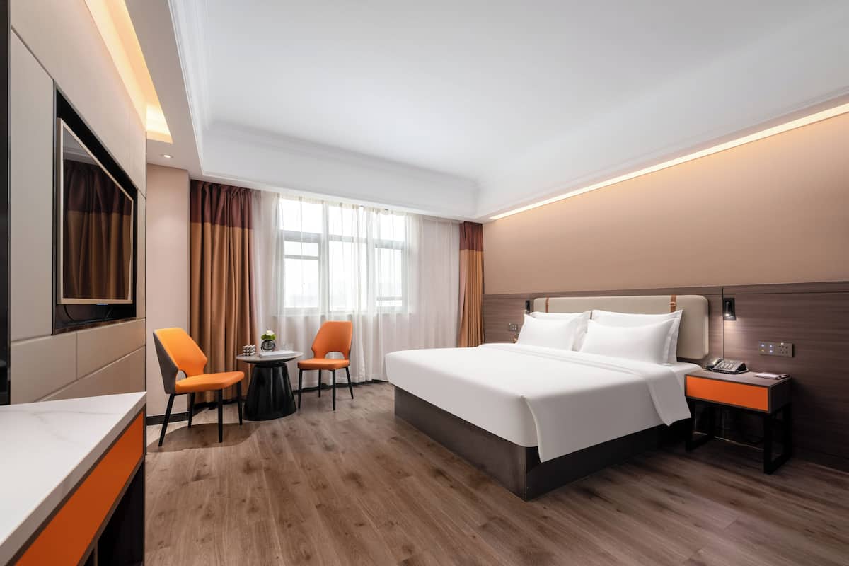 A modern hotel room with a large bed, a desk, a chair, a small table, and a TV.
