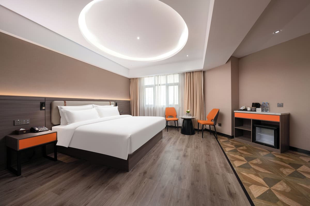 A modern hotel room with a large bed, a desk with a computer, a chair, and a small table with a plant.