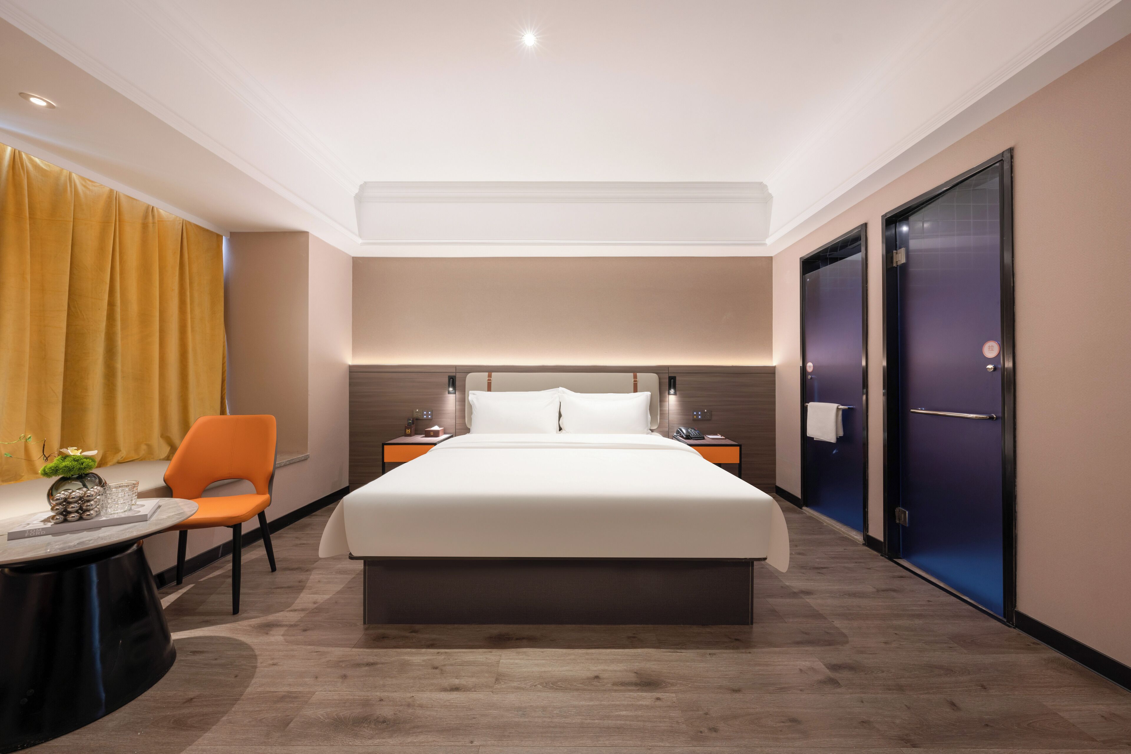Habitación de hotel moderna con una cama grande, un escritorio con silla, una mesita con un florero y una mesita de noche con lámpara.