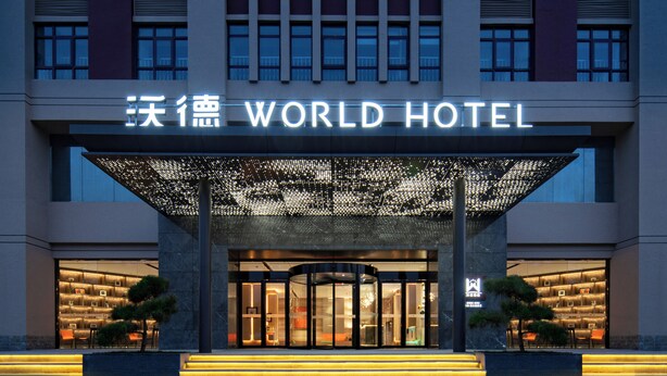 The exterior of the World Hotel with a modern entrance, illuminated signage, and a well-lit facade.