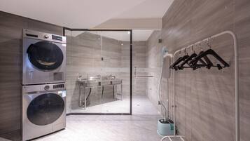 A modern bathroom with a built-in washer and dryer, a glass shower enclosure, and a towel rack.