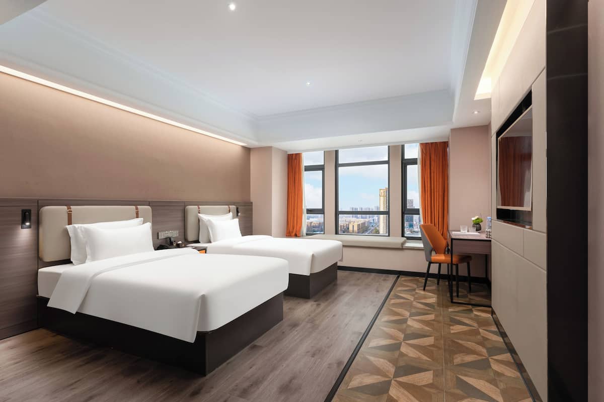 A hotel room with two beds, a desk, a chair, a TV, and a window with curtains.