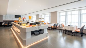 A modern hotel dining area with a central island, seating arrangements, and large windows.