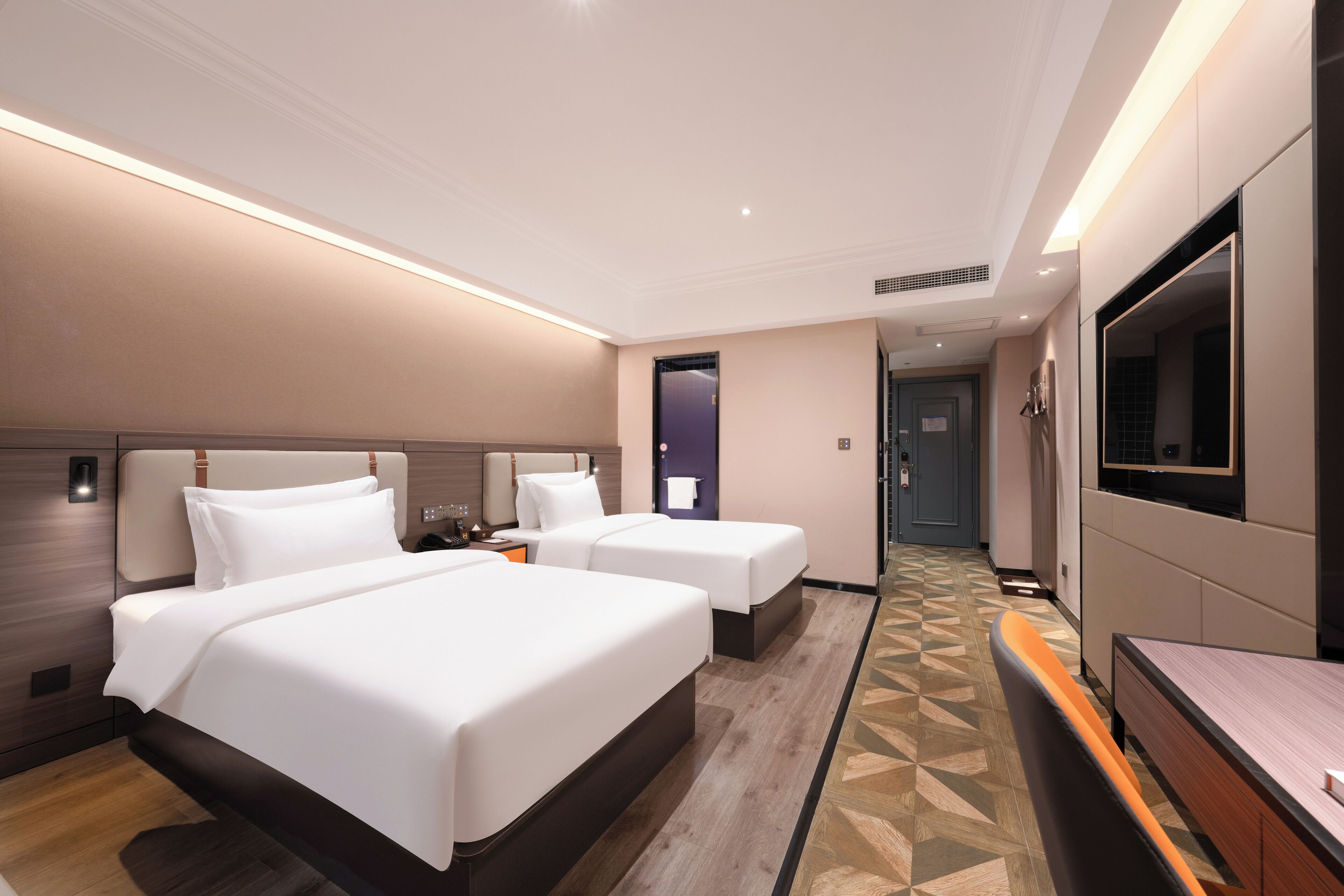 A hotel room with two beds, a TV, a desk, and a patterned floor.