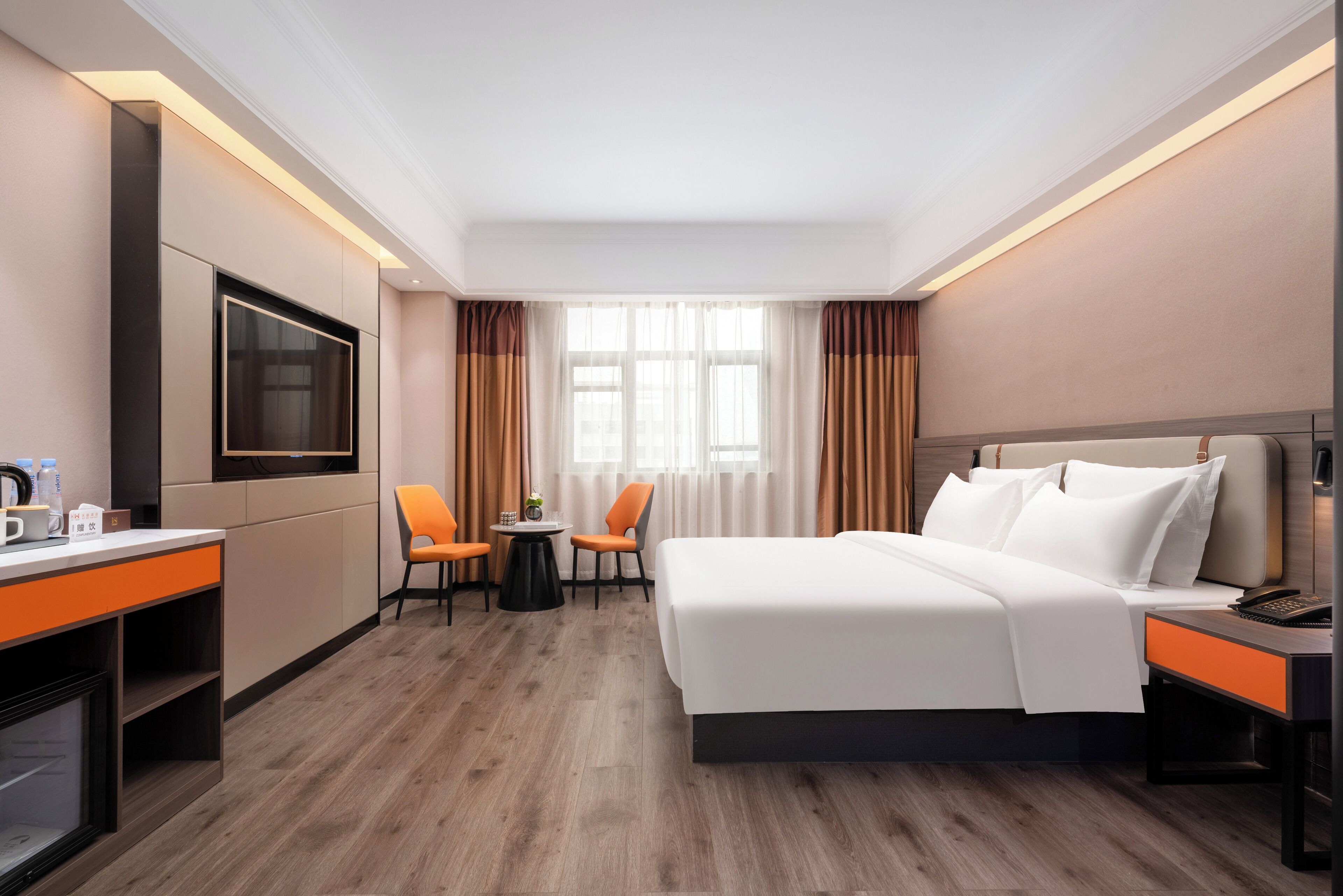 A hotel room with a large bed, a desk with a chair, a small table with two chairs, a television, and a window with curtains.