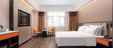 A hotel room with a large bed, a desk with a chair, a small table with two chairs, a television, and a window with curtains.