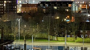 Ein Stadtbild bei Nacht, dominiert von einem Turm mit rotem Leuchtfeuer, umgeben von Gebäuden und einem Parkplatz.