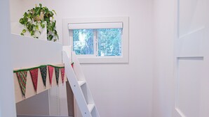 A compact bedroom with a bunk bed, a ladder, a small window, a woven basket, and a patterned rug. - Bird House: Fully Renovated Vesuvius Cottage (Salt Spring Island)