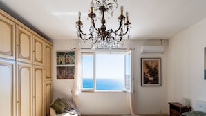 A bedroom with a large window, a chandelier, and a bed with a patterned bedspread. - Casa Cycas by Interhome (Ospedaletti)