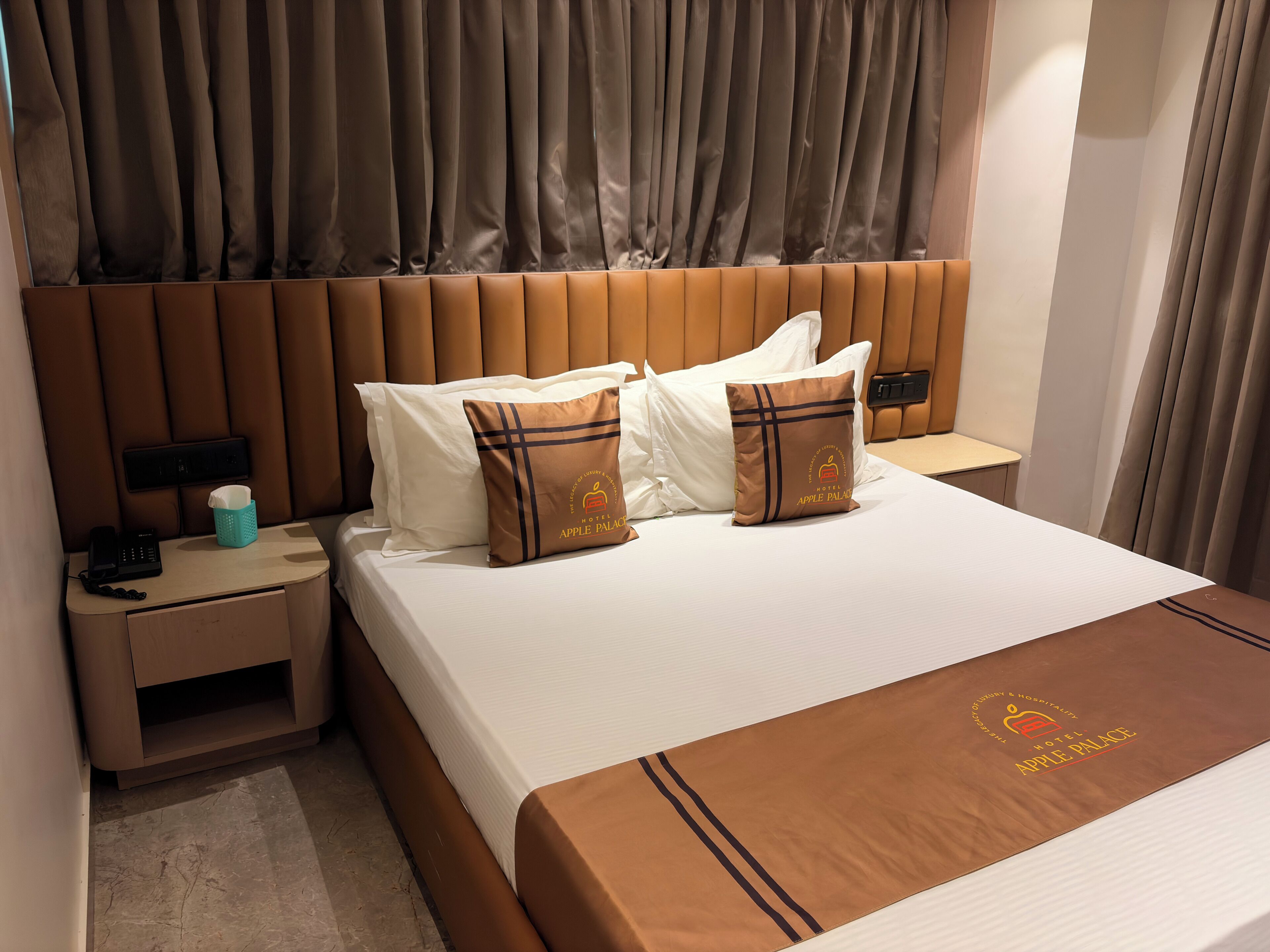 Habitación de hotel con cama, almohadas, mesita de noche, teléfono y caja de pañuelos.
