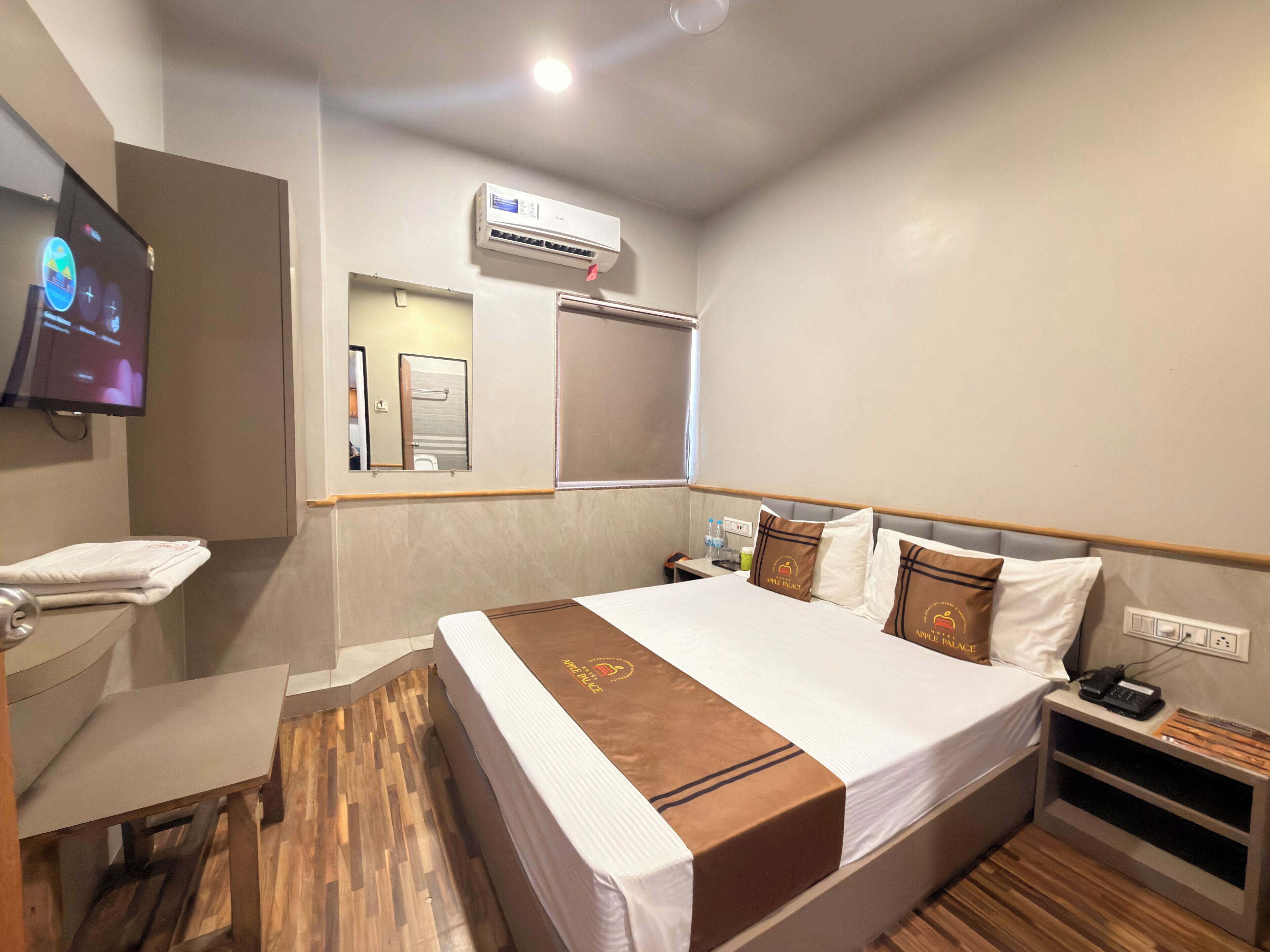 Habitación de hotel con cama, televisor, aire acondicionado, espejo, mesita de noche y velador.